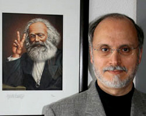 Gilbert Achcar met op achtergrond cartoen afbeelding Marx met V-teken
